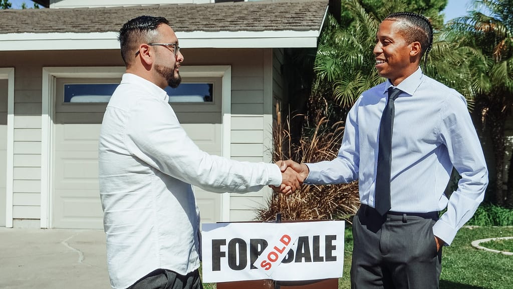 An investor and realtor shaking hands in front of a sold property